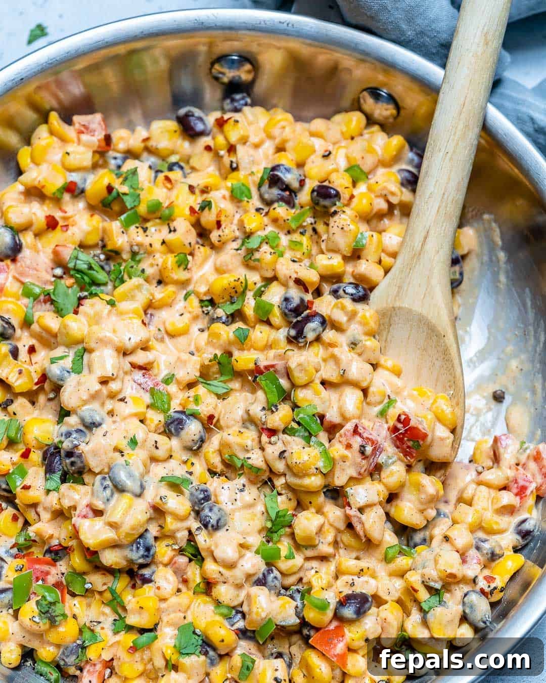Mexican Corn Salad Recipe Creamy Mexican Street Corn Salad in a skillet, garnished with fresh cilantro and a lime wedge.