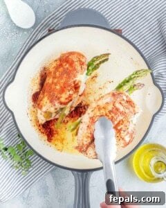 tongs grabbing cooked chicken breast stuffed, in a pan.