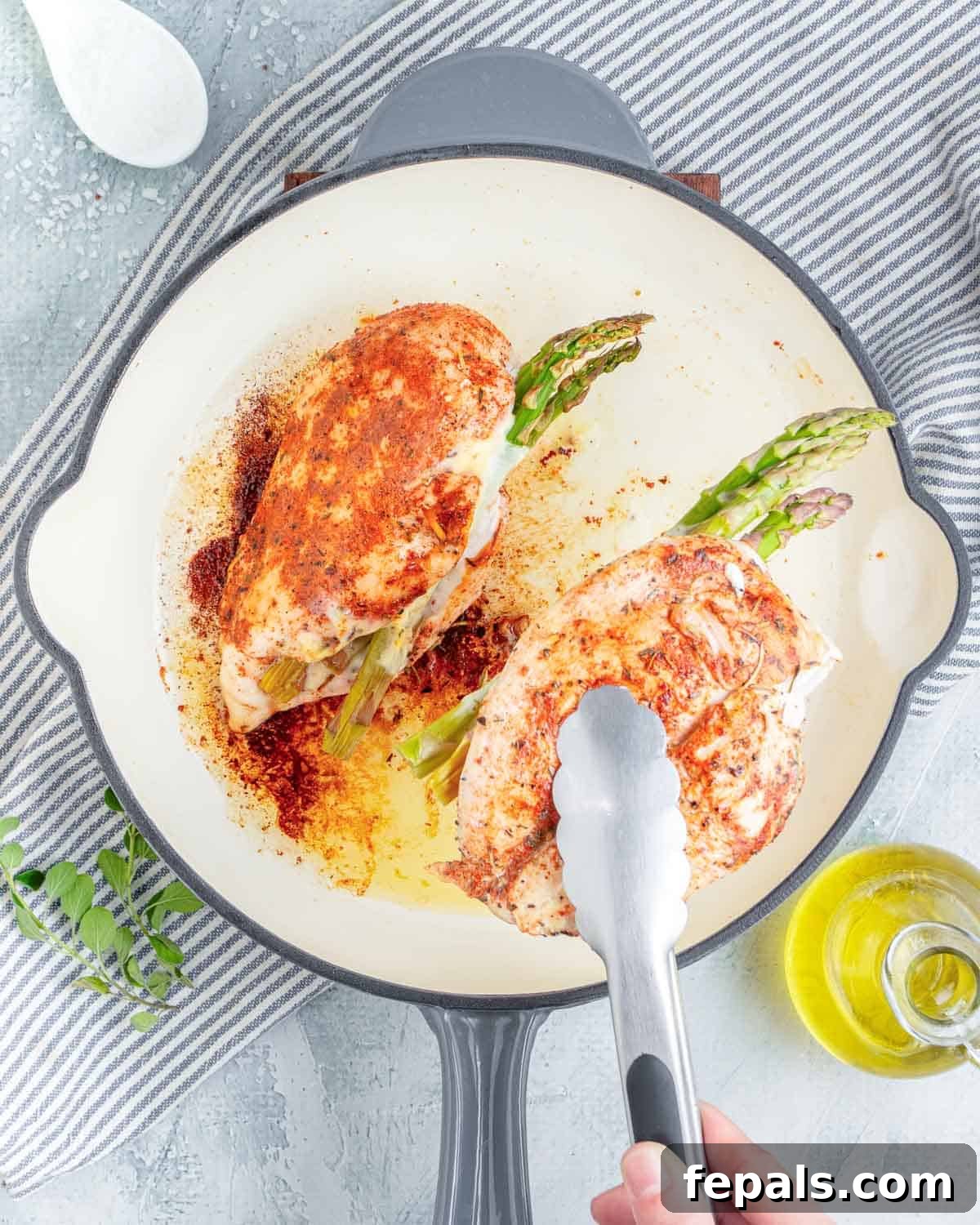 tongs grabbing cooked chicken breast stuffed, in a pan.