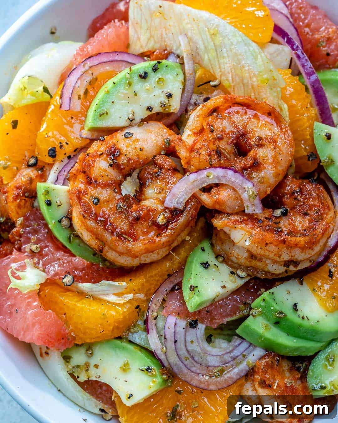 A close-up of a Citrus Cajun Shrimp Salad in a white dish, showcasing succulent shrimp and perfectly sliced avocados.