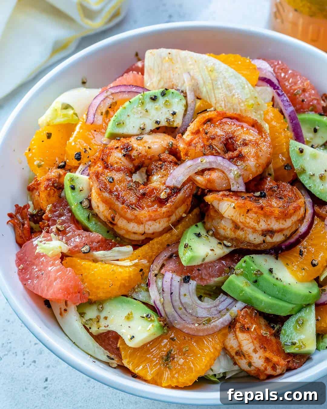A stunning round white bowl filled with Citrus Cajun Shrimp Salad, featuring plump shrimp, vibrant avocados, and bright slices of oranges and grapefruit.