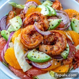 Cooked shrimp in a bowl with slices of oranges, grapefruits, and avocado, part of the Citrus Cajun Shrimp Salad.