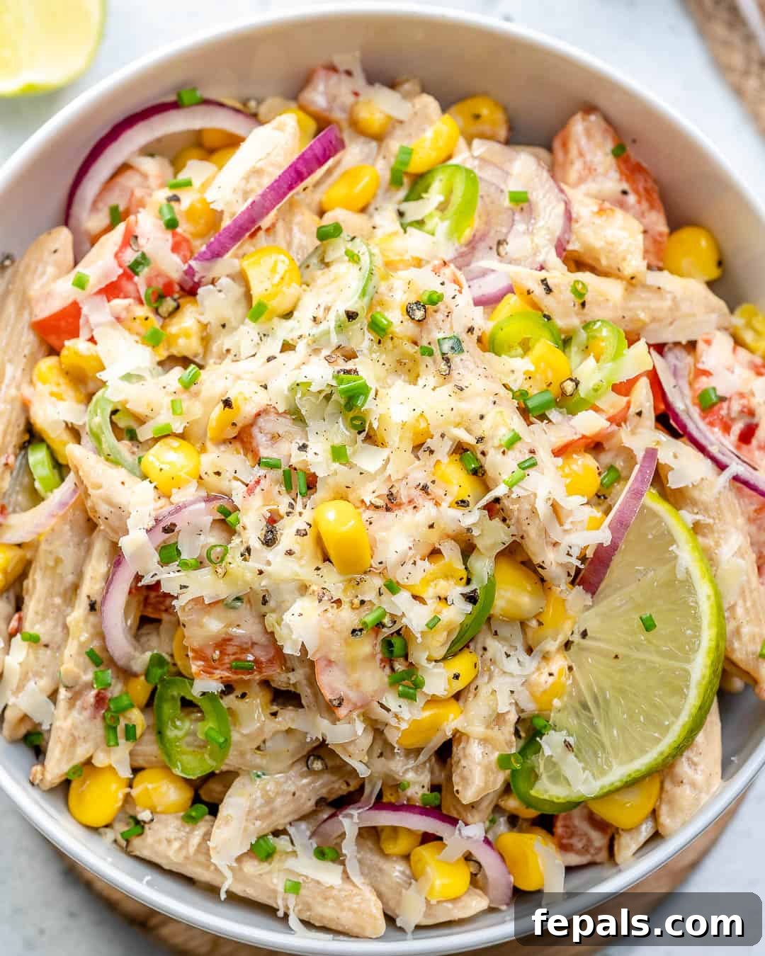 Pasta salad in a bowl topped with shredded cheese and lime garnishes.