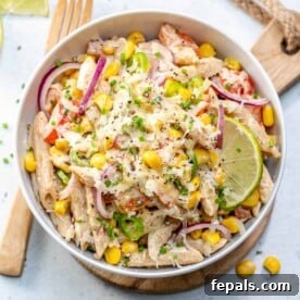 Mexican-style pasta salad in a round bowl, topped with shredded cheese and lime wedges.