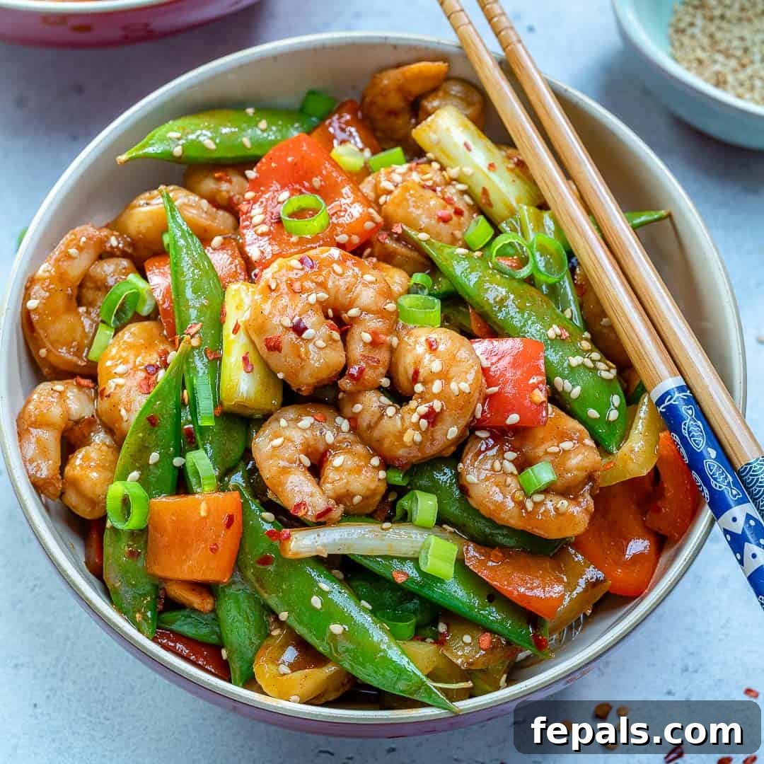 Close-up of Szechuan shrimp stir-fry in a bowl, garnished with green onions and sesame seeds.