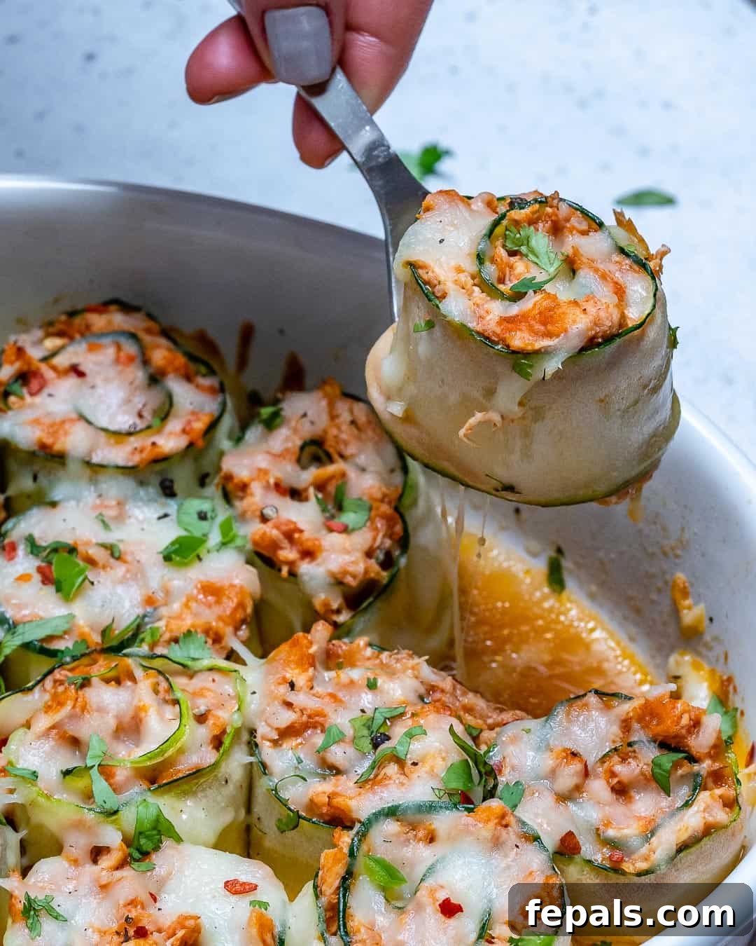 A perfectly rolled chicken enchilada being lifted from the baking dish with a serving spoon, showing its creamy filling.