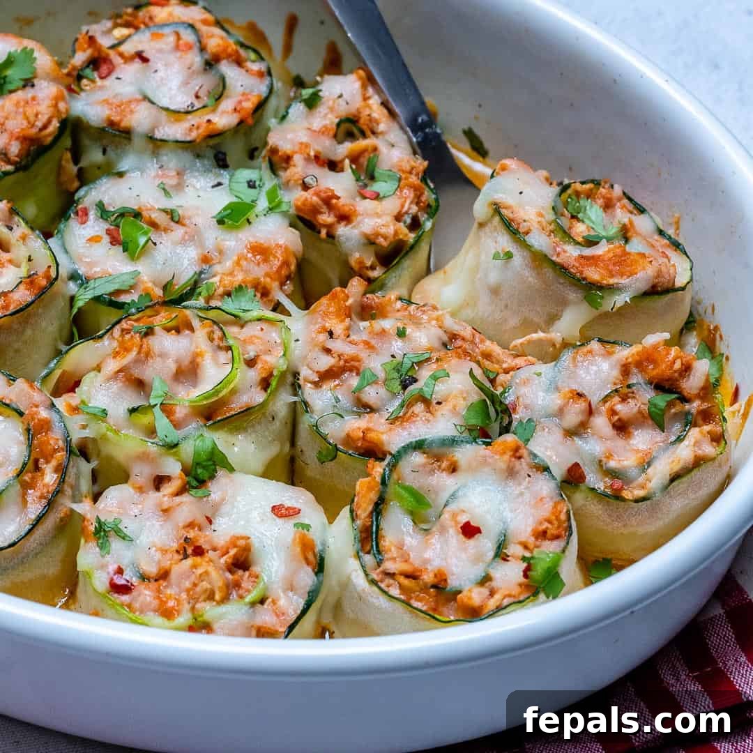 Side shot of perfectly baked zucchini enchilada roll-ups in a white casserole dish, with melted cheese.