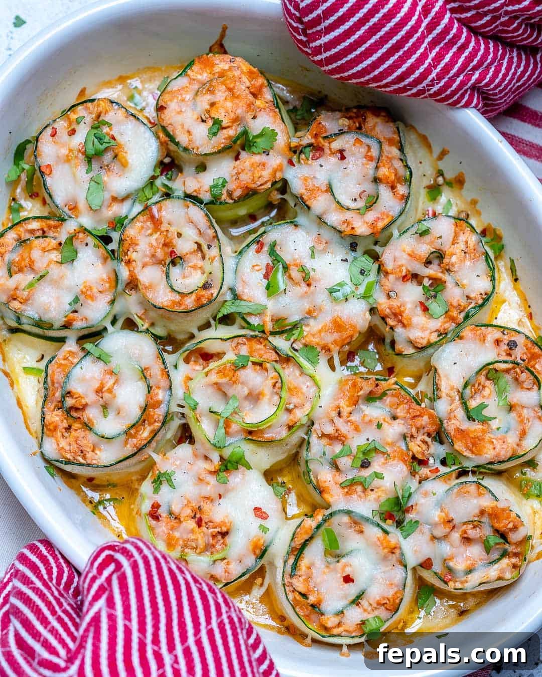 An oven mitt holding a baking dish filled with golden-brown zucchini enchilada roll-ups, fresh out of the oven.