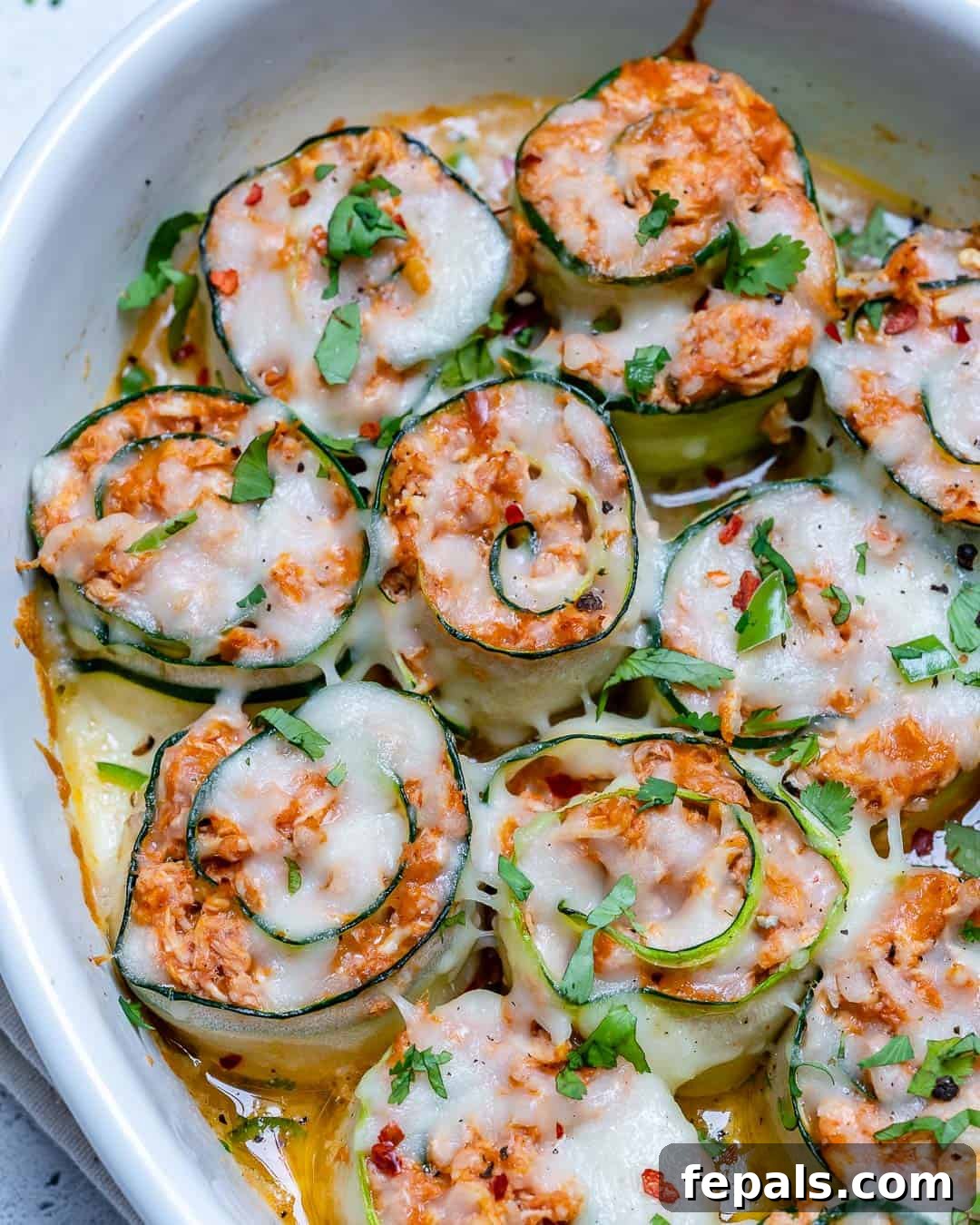 Close-up of a single zucchini enchilada roll-up, showing the rich chicken stuffing and melted cheese, in a white dish.
