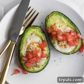 Avocado Egg Nests 6 two stuffed avocado with eggs topped with tomatoes on a plate with fork and knife.
