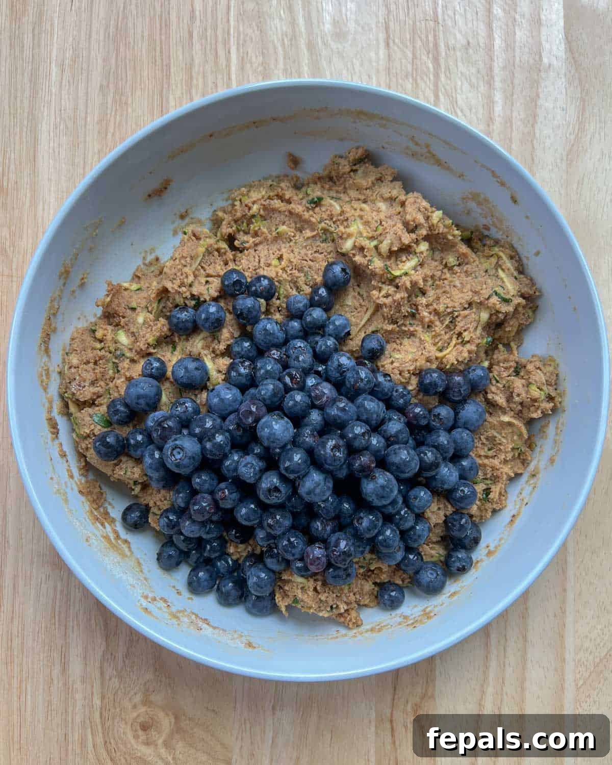 Delicious Blueberry Zucchini Bread 8 Fresh blueberries are carefully folded into the zucchini bread batter in a round mixing bowl.