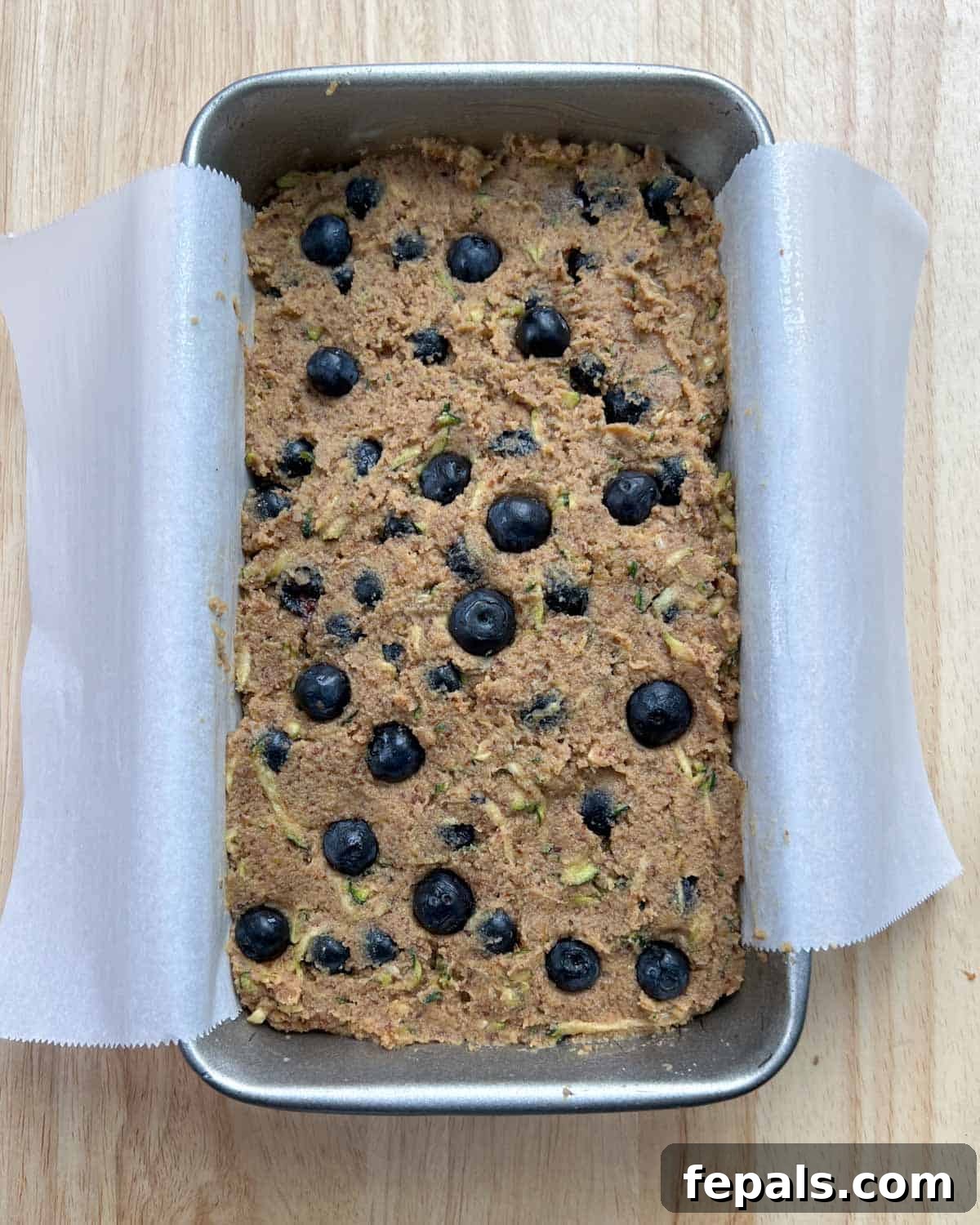 Delicious Blueberry Zucchini Bread 9 The zucchini and blueberry batter is poured into a loaf pan lined with parchment paper, ready for baking.