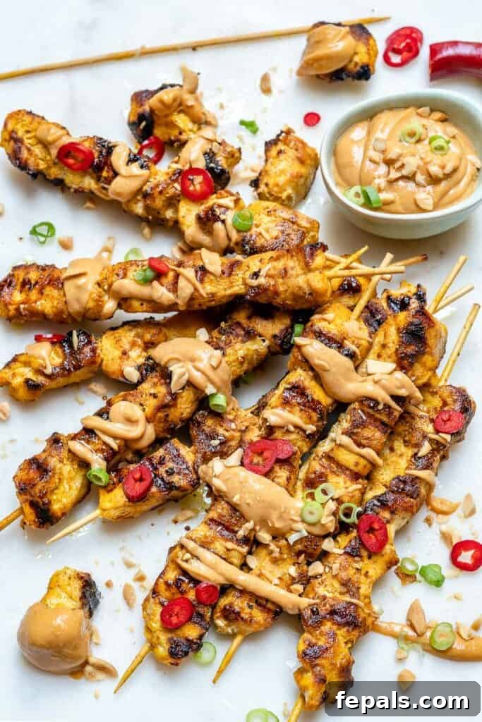 top view of chicken satay skewers on a flat surface with peanut dipping sauce