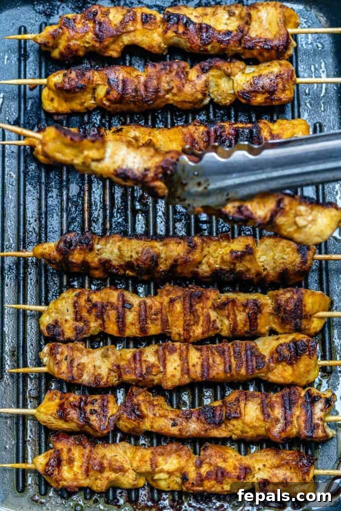 grilled chicken skewers on a grill pan with tong hold one chicken skewer