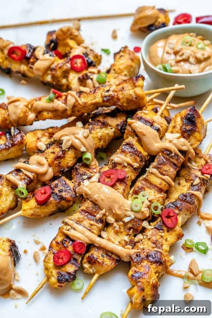 side shot of chicken satay skewers on a flat surface and a drizzle of peanut sauce