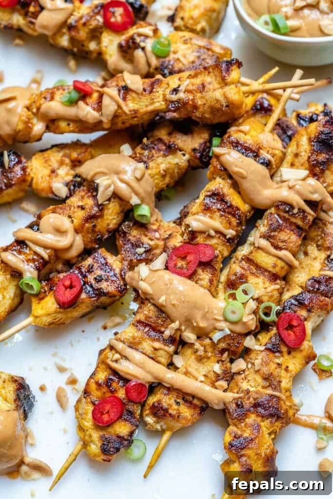 thai chicken skewers on a flat surface with peanut sauce drizzled all over it 
