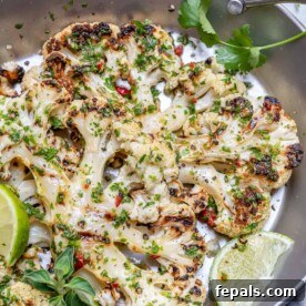 Cauliflower steak on a stainless steel pan with lime wedges topped with chimichurri sauce.