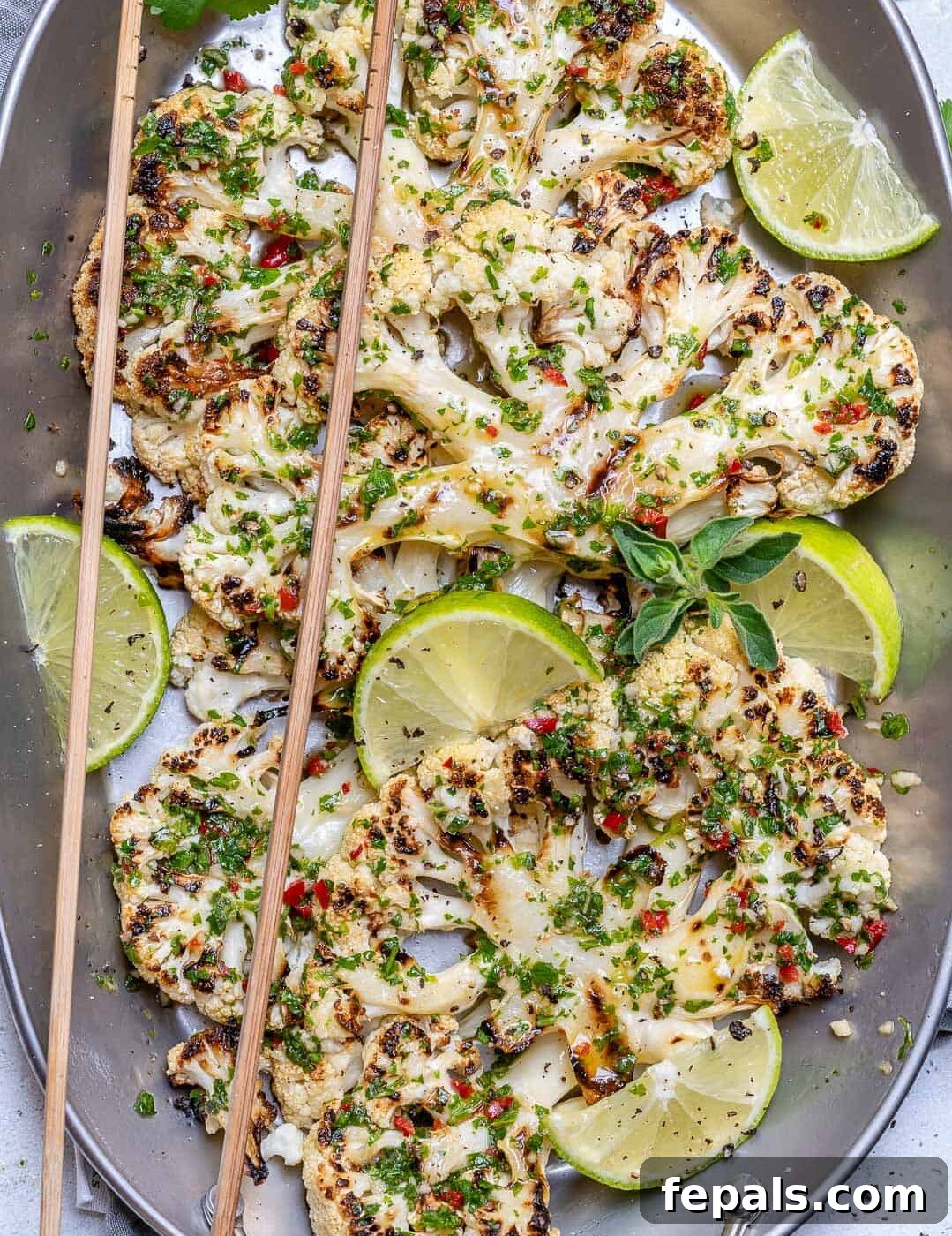 Chargrilled Cauliflower Steaks with Fresh Chimichurri 3 Cauliflower steaks arranged in a pan, ready to be served, with chopsticks and a generous drizzle of chimichurri sauce.