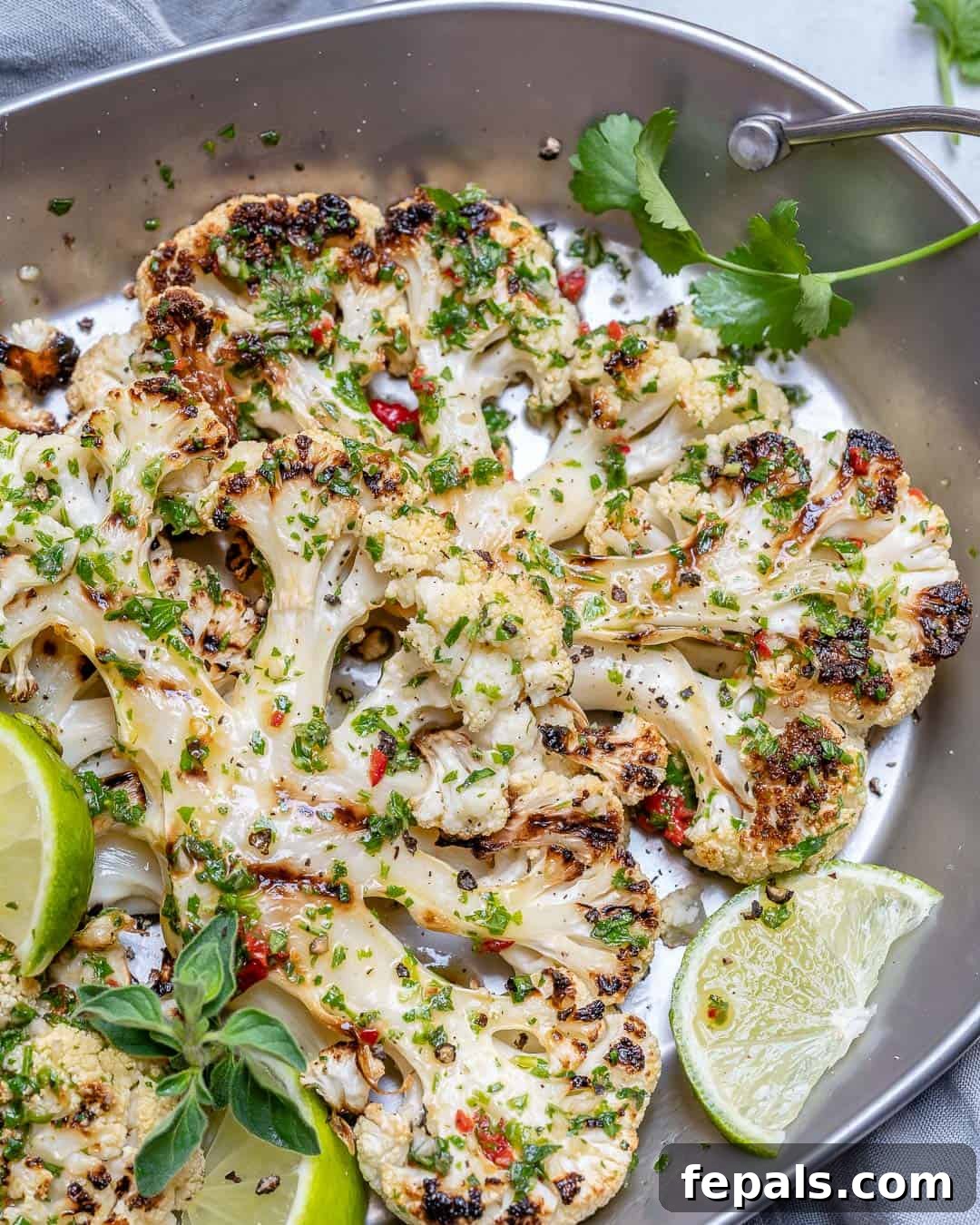 Chargrilled Cauliflower Steaks with Fresh Chimichurri 9 Grilled cauliflower steak served on a stainless steel pan, garnished with fresh lime wedges and a generous topping of chimichurri sauce.
