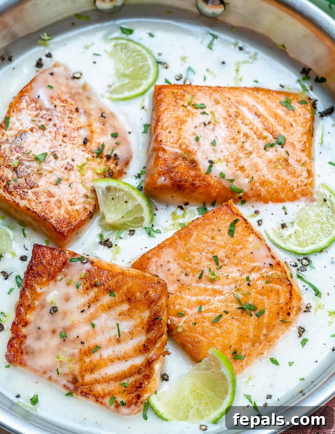 4 seared salmon in a creamy white sauce in a pan.