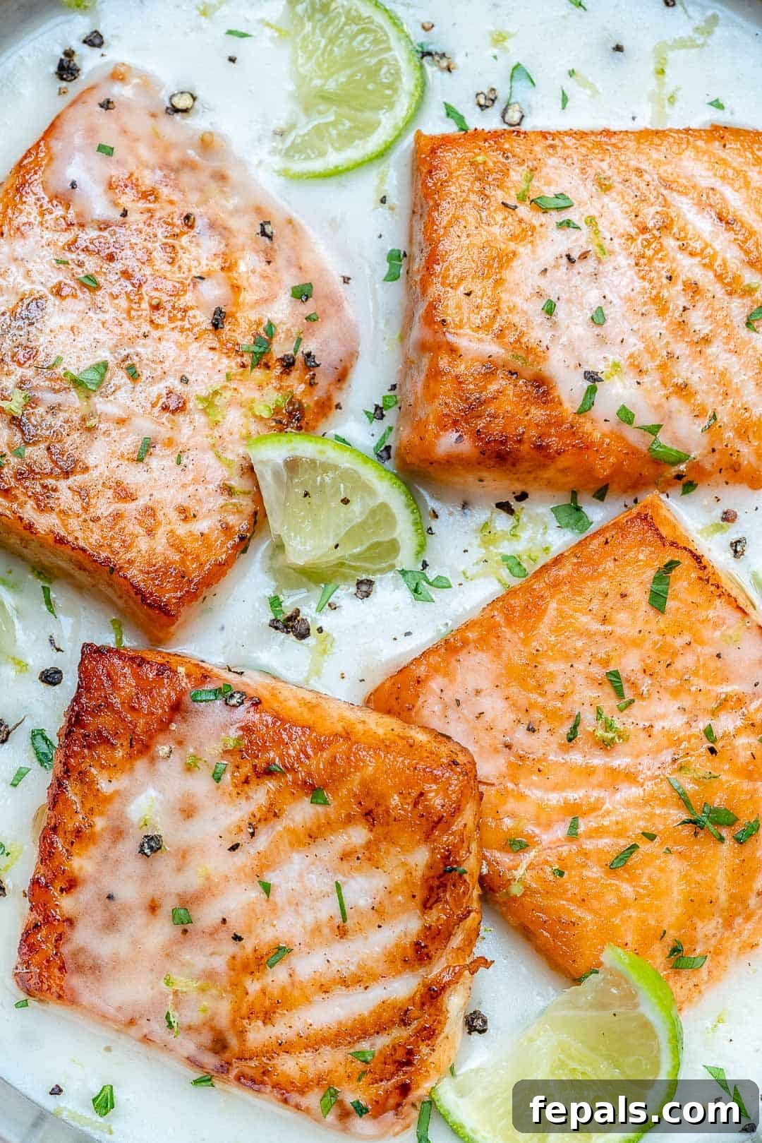 4 seared salmon filets in a creamy white sauce in a skillet.