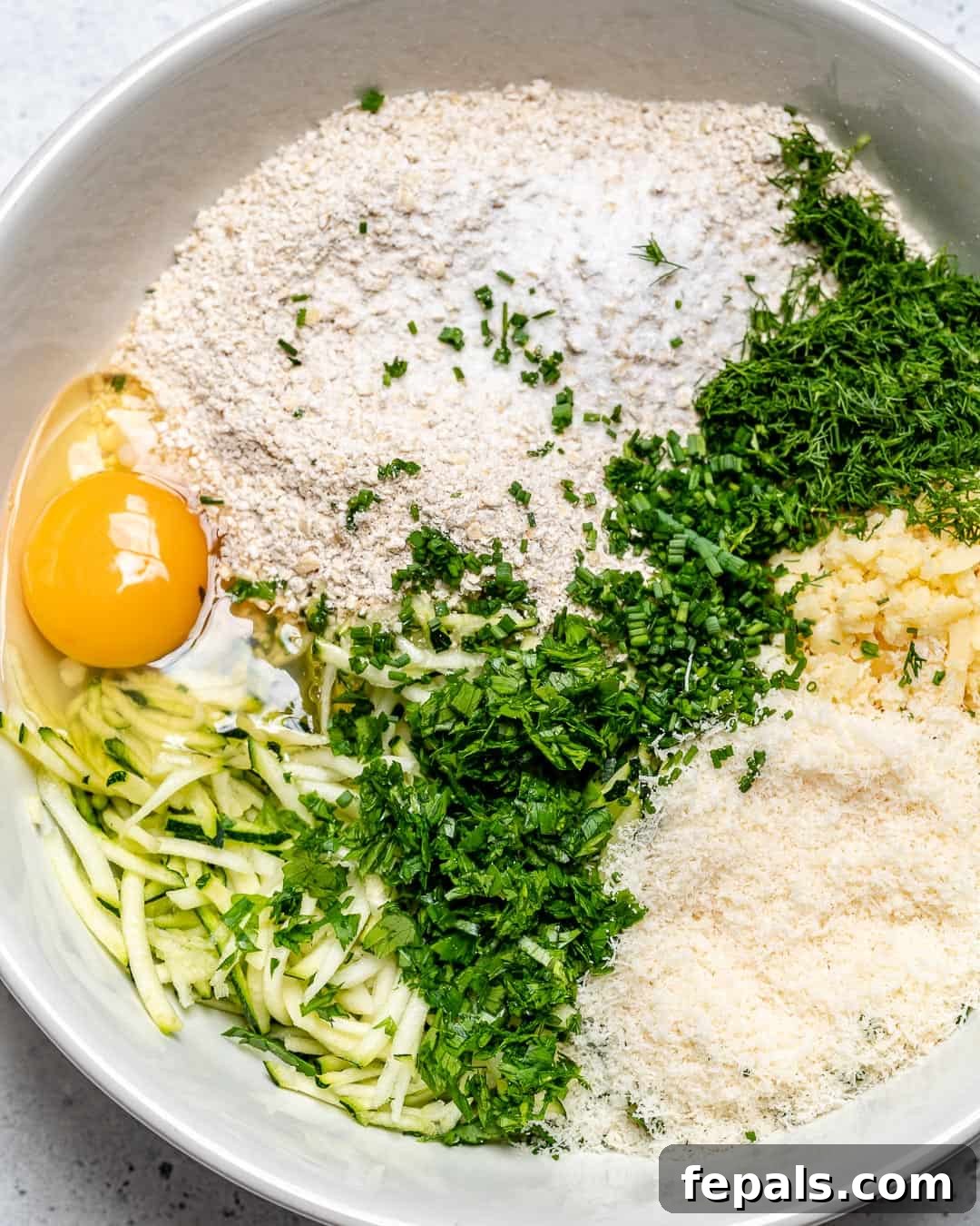 Savory Baked Garlic Herb Zucchini Fritters 3 hands mixing zucchini fritter batter in a bowl