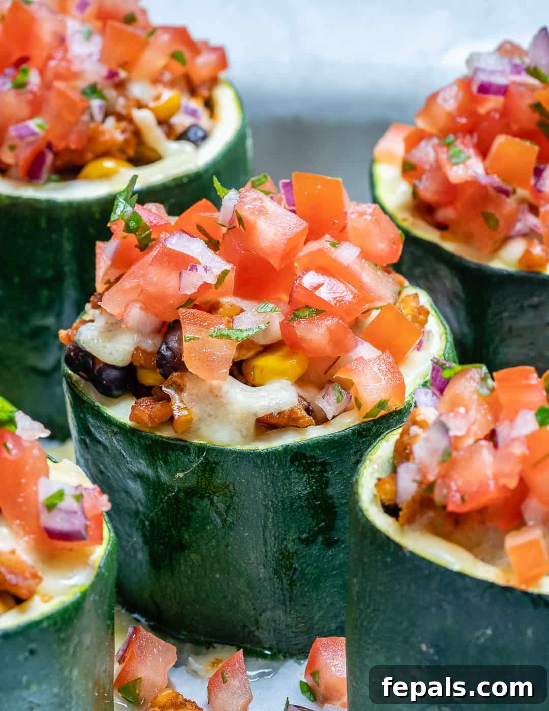 Loaded Zucchini Tacos 3 Close-up view of zucchini cups filled with cooked taco-seasoned ground beef or turkey, garnished with chopped tomatoes and cilantro.