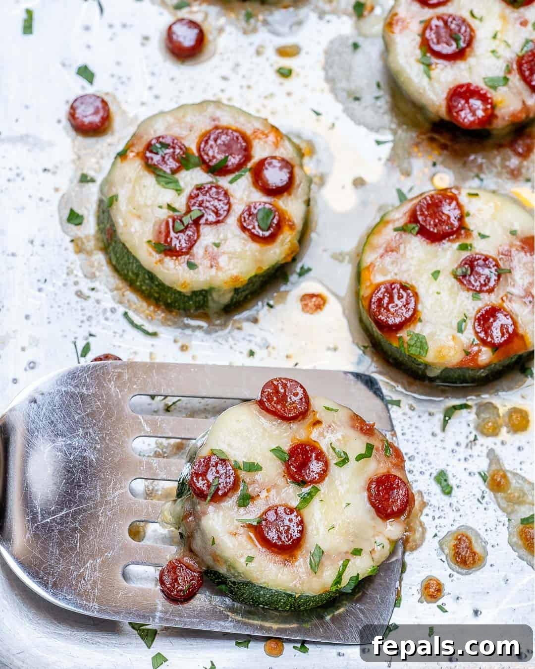 Zucchini Pizza Poppers 3 spatula getting a cheesy pizza zucchini bite from a baking sheet.