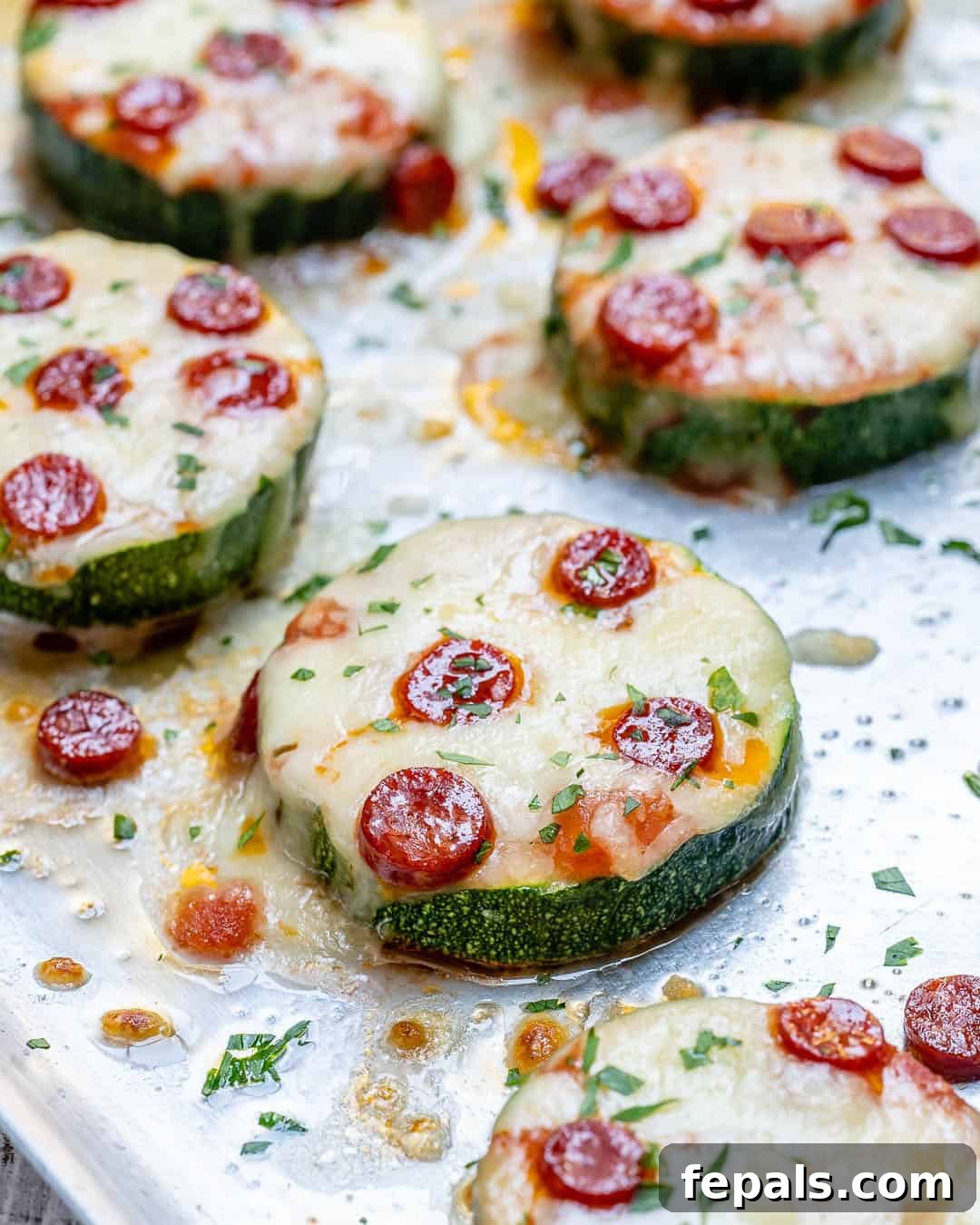 Zucchini Pizza Poppers 4 pizza zucchini bites topped with pepperoni and melted cheese on a sheet pan, fresh from the oven.