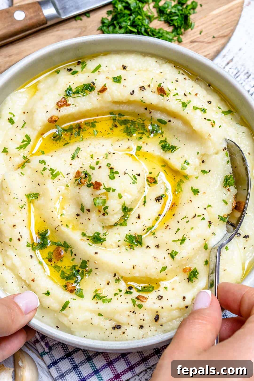 Whipped Garlic Butter Cauliflower 4 A hand holding a spoon, scooping a generous portion of creamy mashed cauliflower from a bowl, showcasing its smooth texture.
