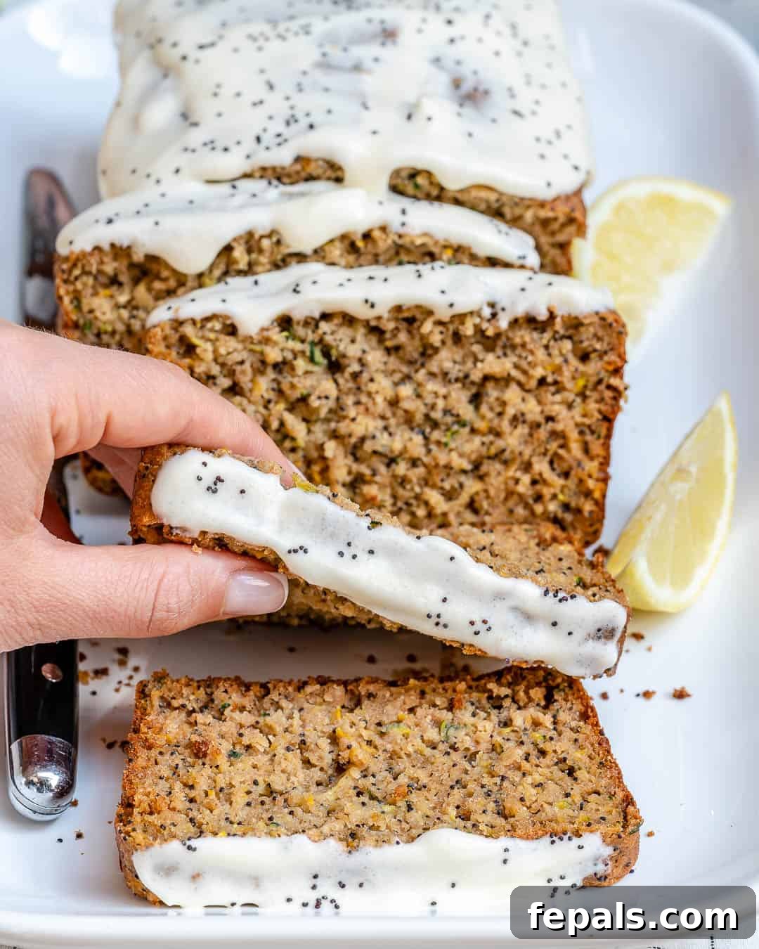 A hand reaching for a slice of moist lemon poppy seed zucchini bread topped with glaze.