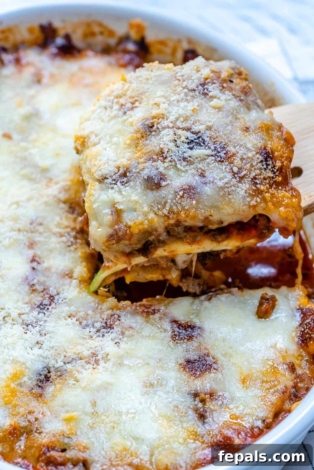 Satisfying Zucchini Lasagna Bake 13 A tantalizing close-up of a slice of zucchini lasagna being carefully removed from a casserole dish, highlighting its rich layers of meat, cheese, and tender zucchini.