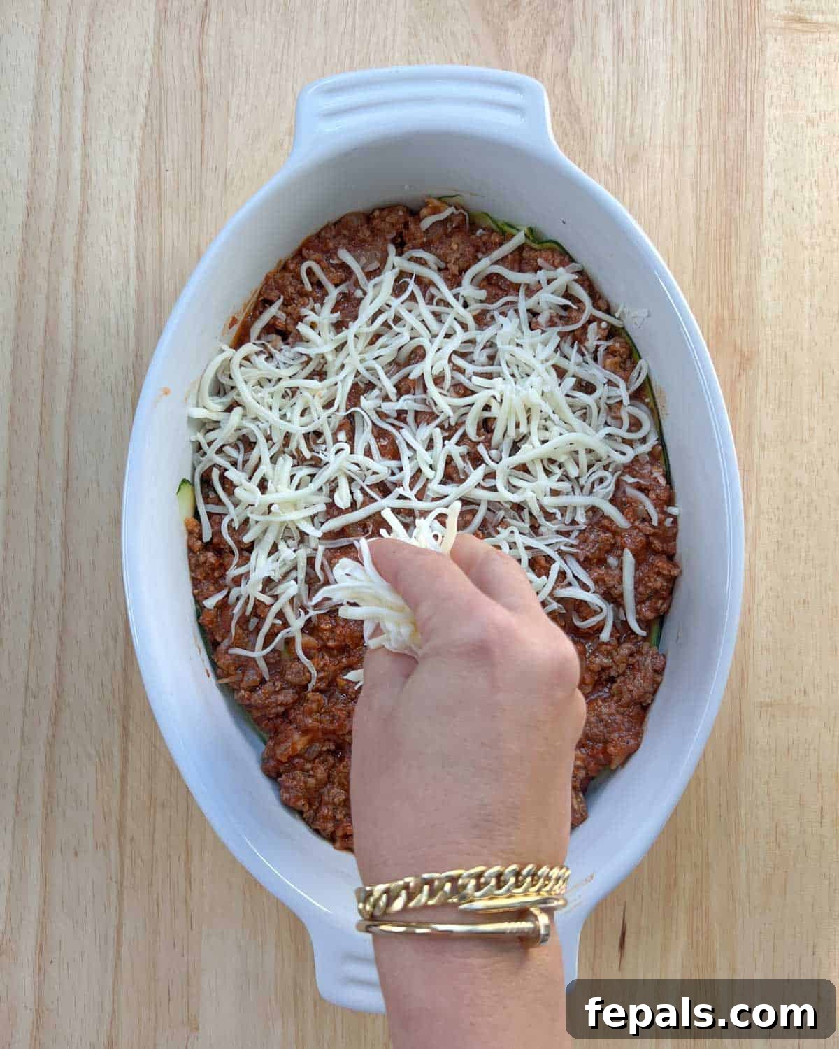 Satisfying Zucchini Lasagna Bake 7 A bountiful layer of shredded mozzarella cheese being generously sprinkled over the rich meat sauce, preparing for the next layer of zucchini.