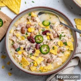 Creamy White Chicken Chili 12 A round bowl with white chicken chili made with four different beans garnished with sliced jalapenos.