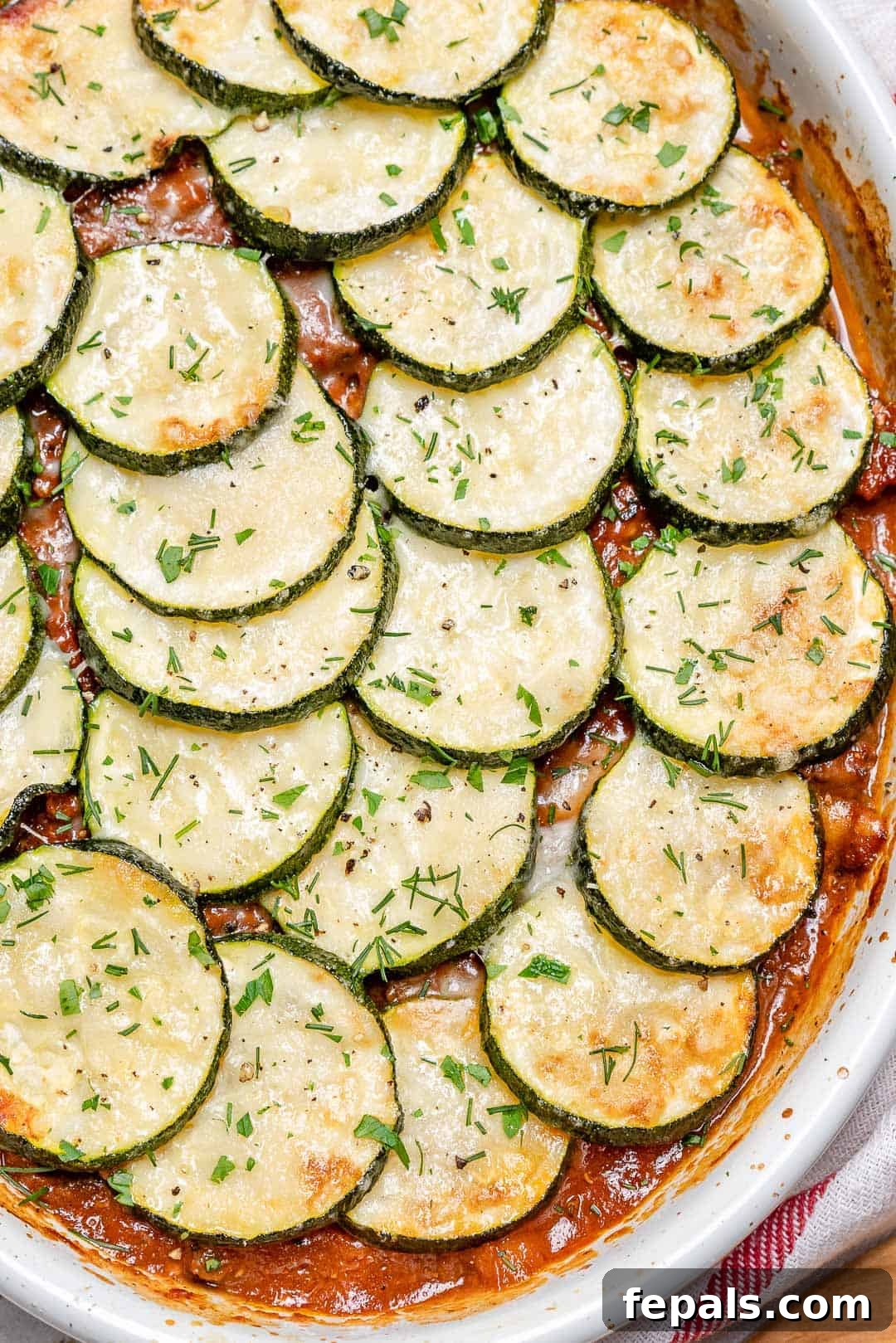 Savory Greek Zucchini Moussaka 4 An oval baking dish showcasing baked moussaka topped with perfectly layered zucchini slices and a golden cheese crust.