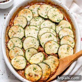 A wooden spoon in a white baking dish with Greek moussaka, emphasizing the healthy layers.