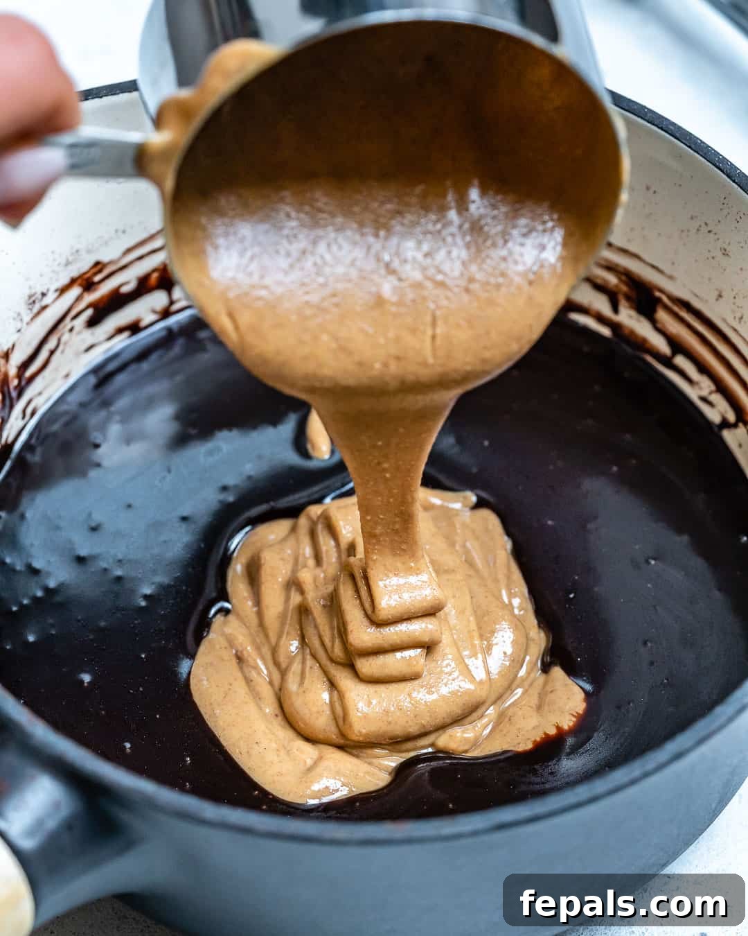Smooth, creamy peanut butter being added to a rich chocolate mixture in a saucepan.