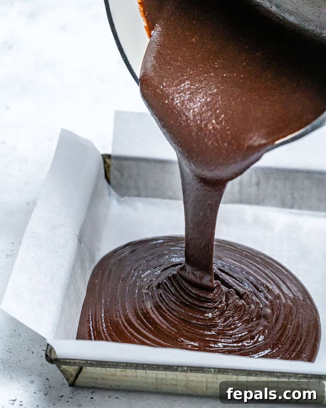 The chocolate and peanut butter fudge mixture smoothly poured into a parchment-lined baking pan, ready for topping.