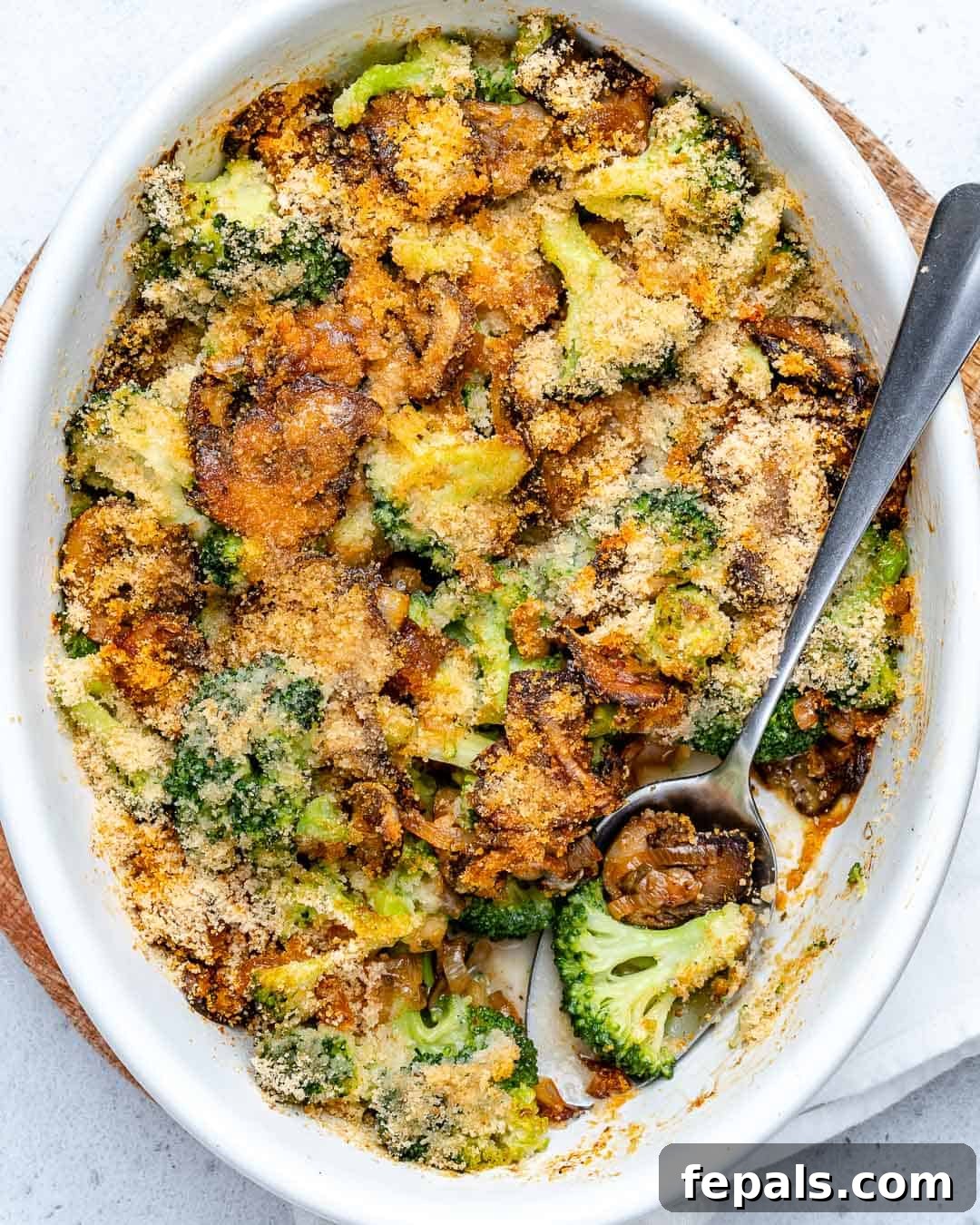A serving spoon carefully placed in a healthy broccoli casserole dish, showcasing the steamed broccoli and sautéed mushrooms within the oval baking dish.