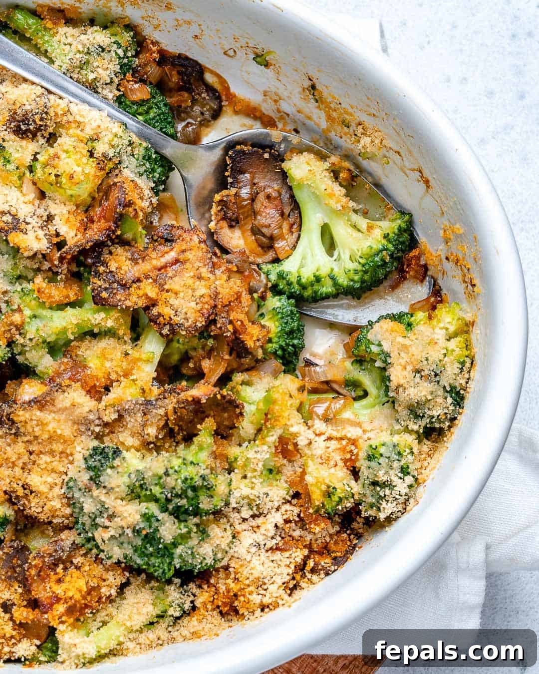 A portion of the cooked broccoli and mushroom casserole visible in a white oval dish, showing the golden-brown topping.