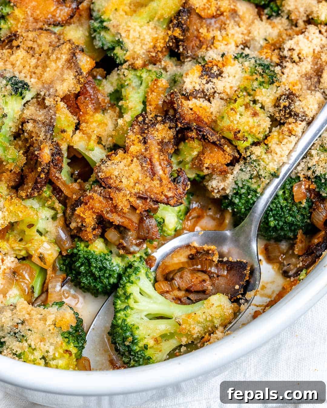 A serving spoon lifting a portion of healthy broccoli casserole with mushrooms from a white oval dish, ready to be enjoyed.