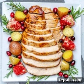 top view of sliced turkey breasts on a white plate with baby potatoes fresh rosemary and pomegranates