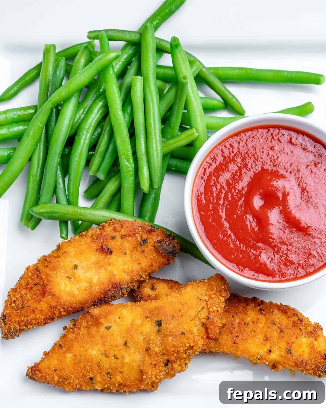 Crispy oven-fried chicken tenders served on a plate with fresh green beans and a small bowl of ketchup for dipping.