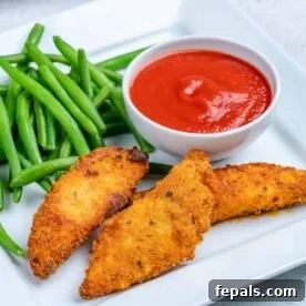 A plate featuring three crispy chicken tenders alongside green beans and a small dish of ketchup.