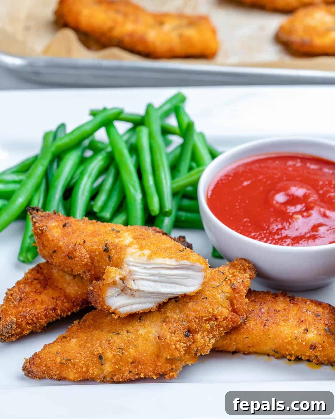 A side view of crispy golden brown chicken tenders arranged on a plate with green beans as a healthy side.