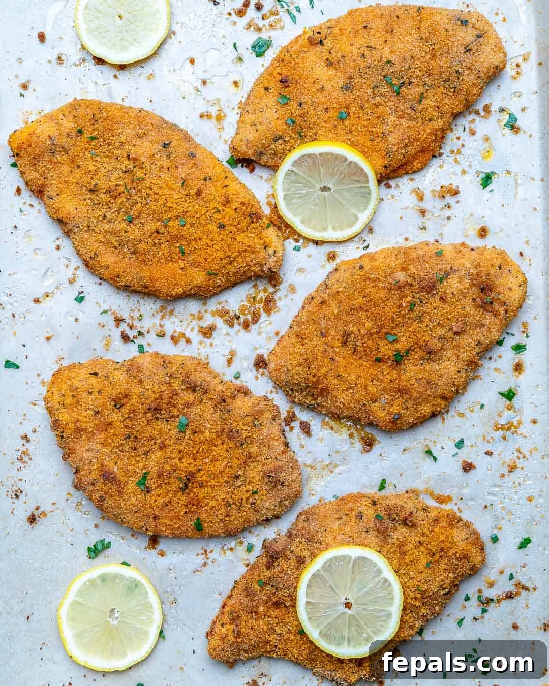Golden Baked Chicken Cutlets 2 overhead view of crispy baked chicken cutlets on a sheet pan, garnished with fresh herbs