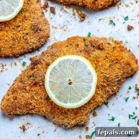 crispy baked chicken cutlet recipe on a white plate with lemon wedges