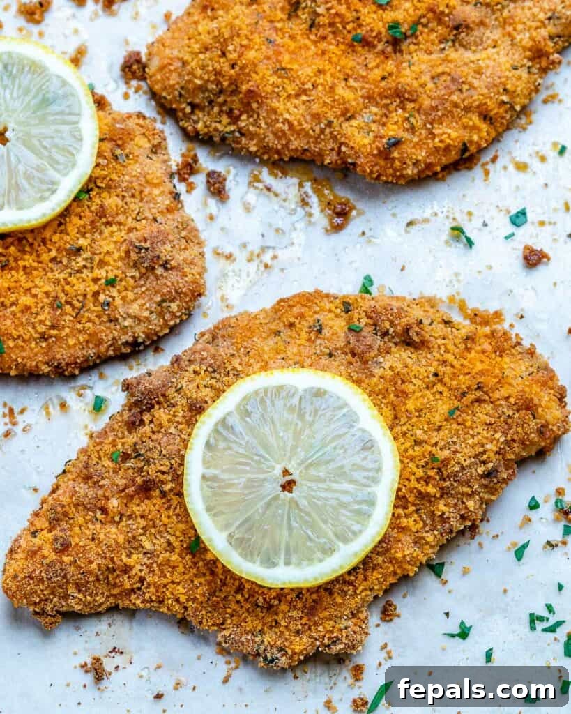 Golden Baked Chicken Cutlets 4 crispy oven fried chicken cutlets with a slice of lemon on a white plate