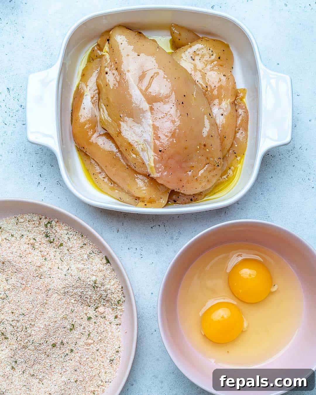 Golden Baked Chicken Cutlets 6 chicken marinated in a bowl, with separate bowls of breadcrumbs and egg wash nearby