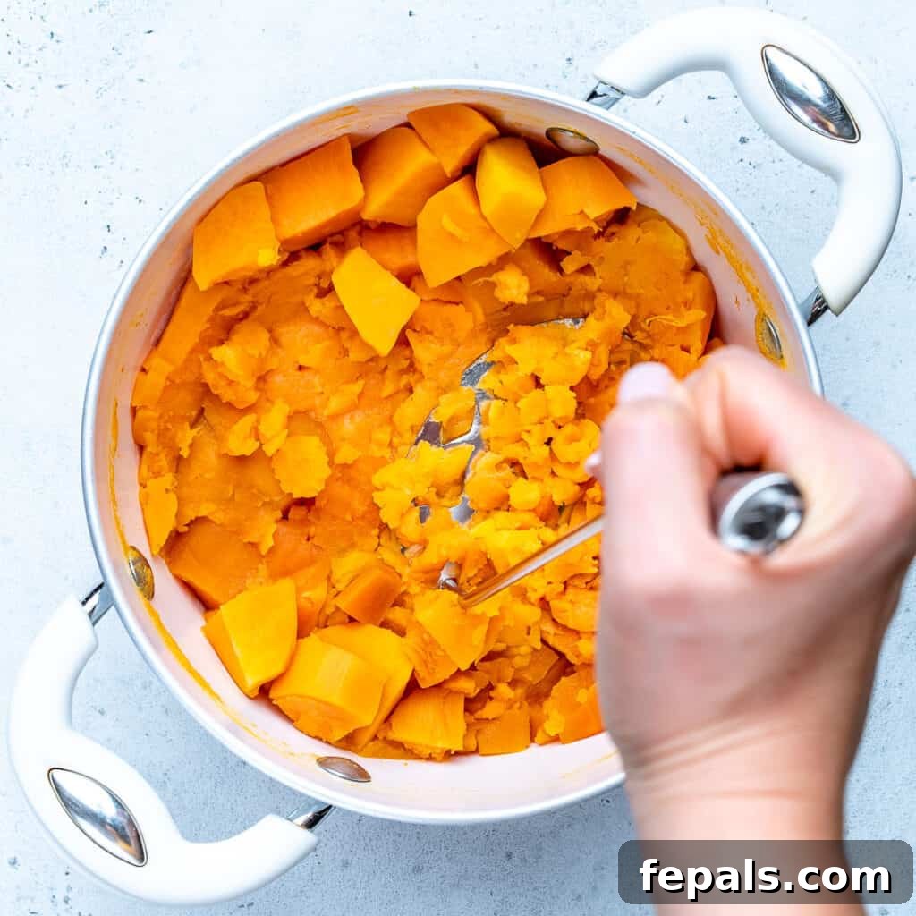 hand mashing the cooked sweet potatoes in a pot